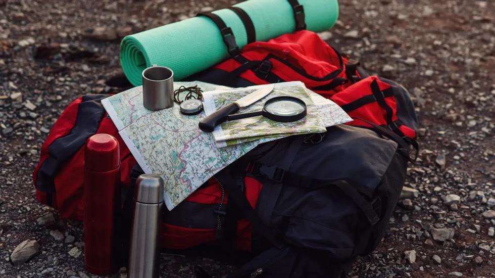 close-up-shot-travel-equipment-backpack-map-compass-knife-sleeping-pad-ground
