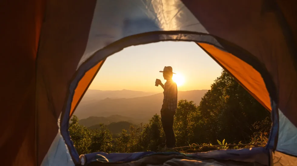 happy-man-with-holding-coffee-cup-stay-near-tent-around-mountains